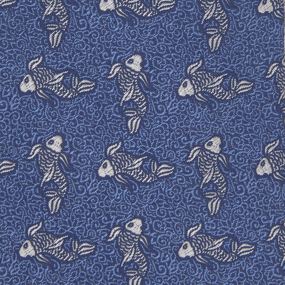 The Blue Carp Silk Tie by Turnbull & Asser features a blue silk base with white and dark blue koi fish among light blue swirls. The tie is displayed rolled up, pointed end forward.
