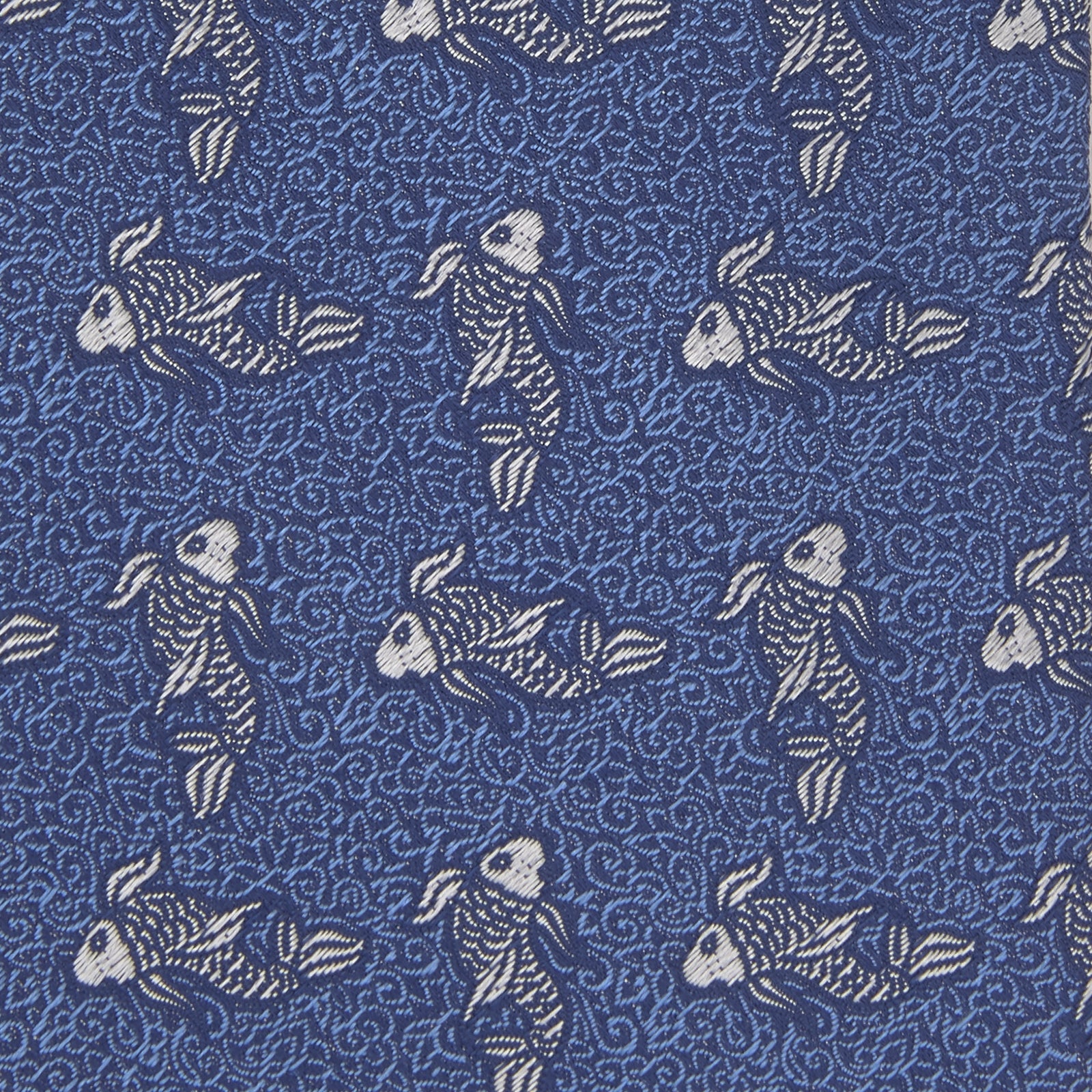 View 3 of product The Blue Carp Silk Tie by Turnbull & Asser features a blue silk base with white and dark blue koi fish among light blue swirls. The tie is displayed rolled up, pointed end forward.