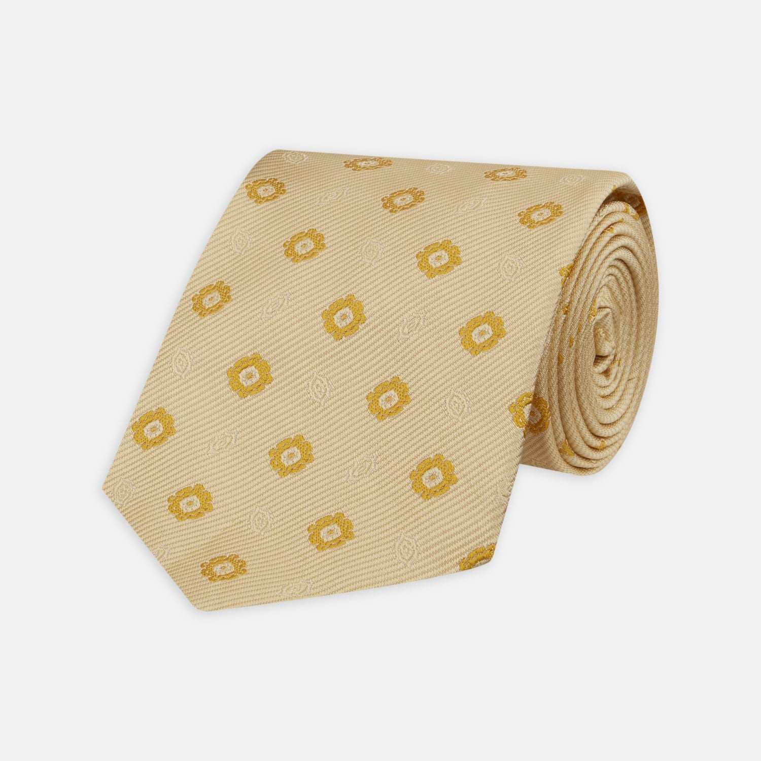 View 1 of product The Turnbull & Asser Soft Yellow Floral Jacquard Stripe Silk Tie features a rolled-up beige design with subtle texture and small yellow floral patterns evenly spaced throughout.