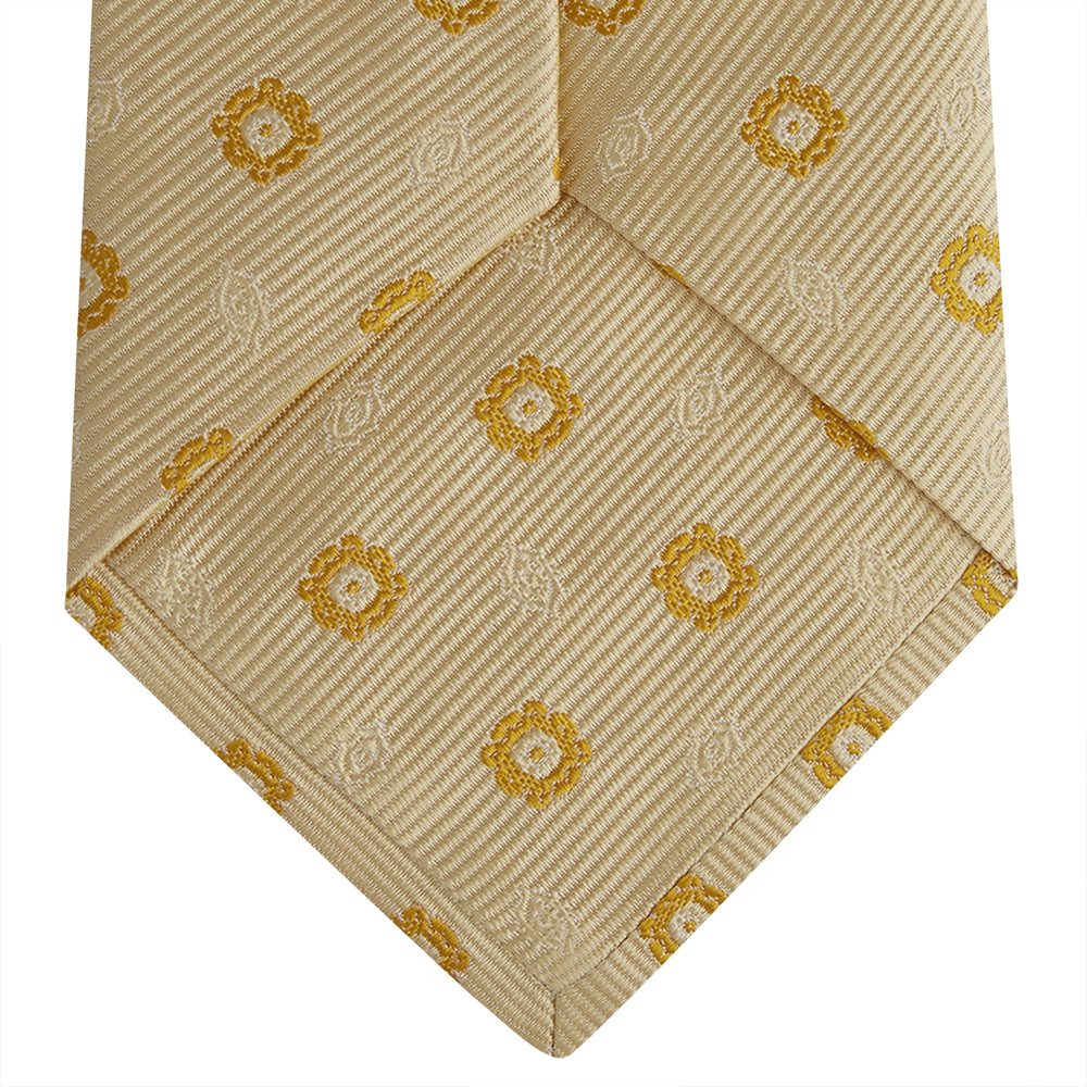 The Turnbull & Asser Soft Yellow Floral Jacquard Stripe Silk Tie features a rolled-up beige design with subtle texture and small yellow floral patterns evenly spaced throughout.