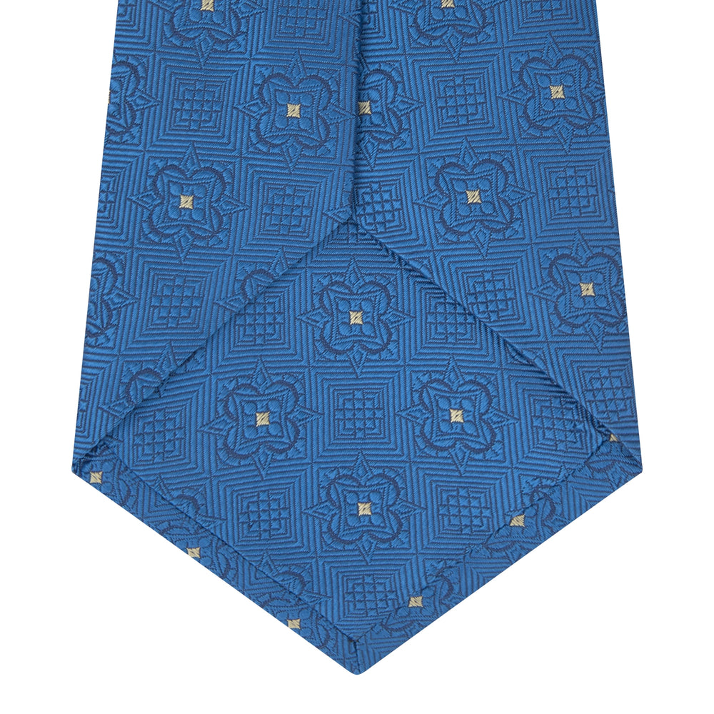 The Turnbull & Asser Blue Flower Mosaic Silk Tie features a blue silk fabric with a detailed geometric and floral design, accented in lighter blue and white, displayed on a white background.