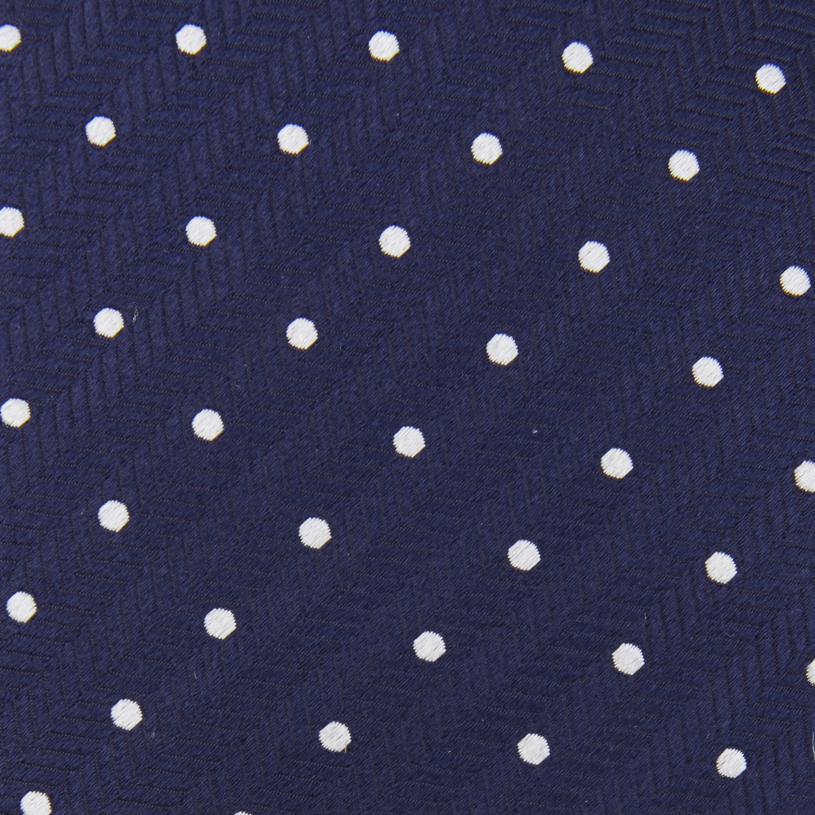 View 3 of product The Turnbull & Asser Slim Navy & White Spot Herringbone Silk Tie features a subtle texture and white polka dots, making it a refined men's accessory. Shown rolled-up on a plain white background.