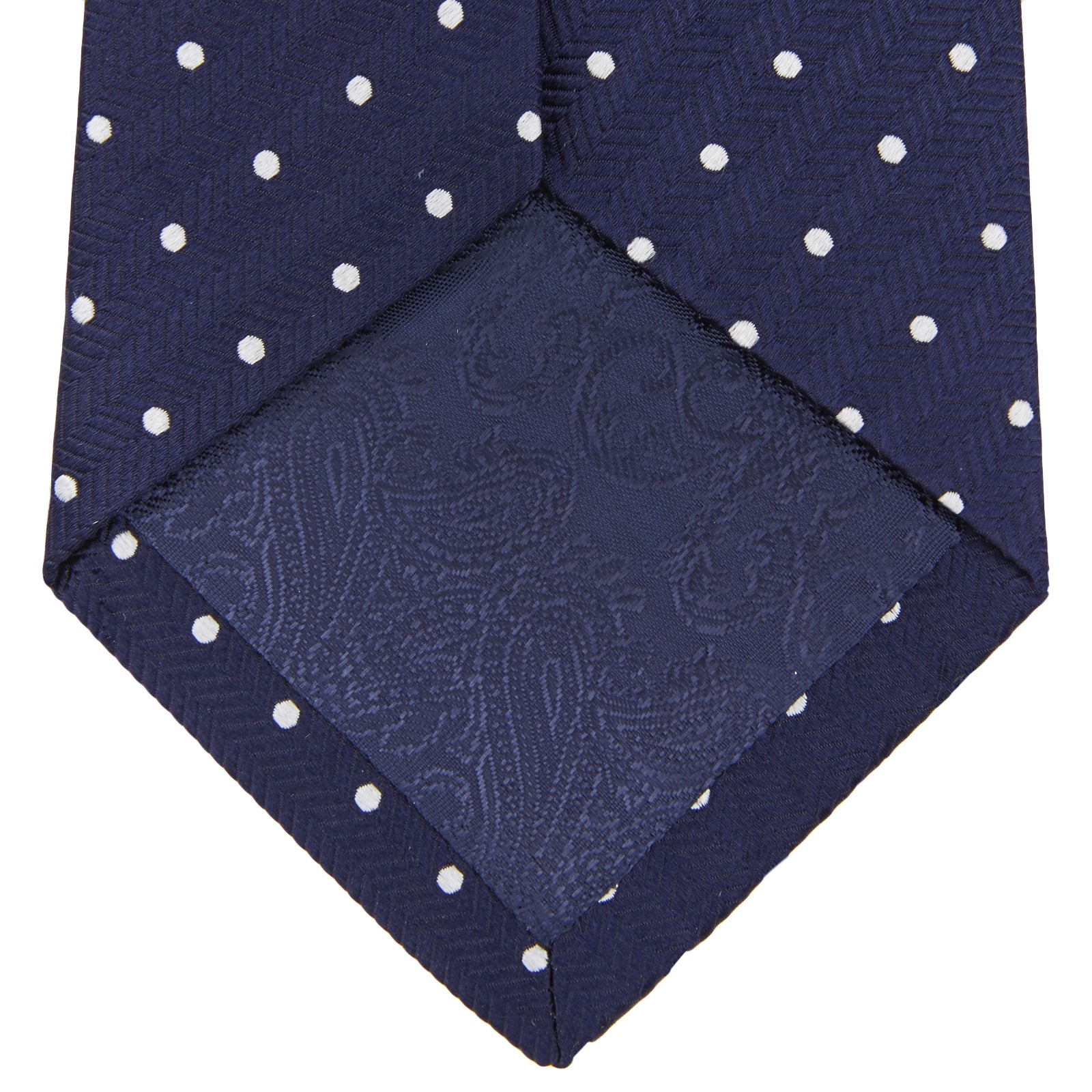 View 4 of product The Turnbull & Asser Slim Navy & White Spot Herringbone Silk Tie features a subtle texture and white polka dots, making it a refined men's accessory. Shown rolled-up on a plain white background.