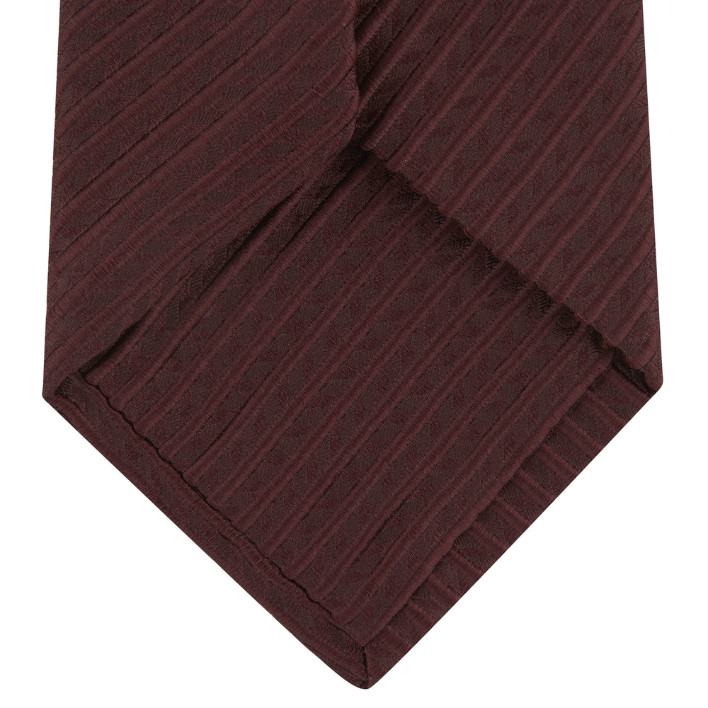 The Turnbull & Asser Burgundy Ottoman Silk Tie features a heavyweight ribbed silk with a subtle diagonal wave pattern, shown rolled up on a plain white background.