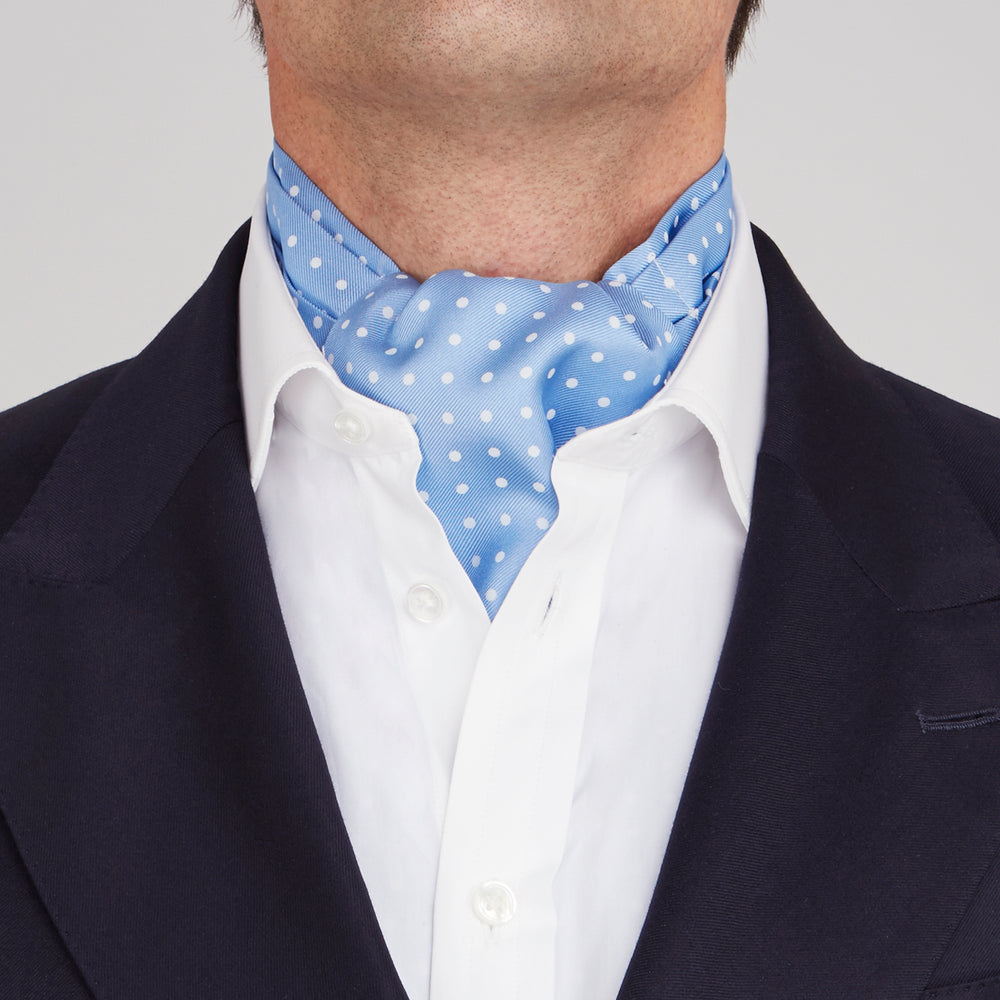 The Turnbull & Asser Sky Blue and White Medium Spot Silk Ascot Tie, neatly folded against a white background, is stylish neckwear—perfect for any wedding guest.